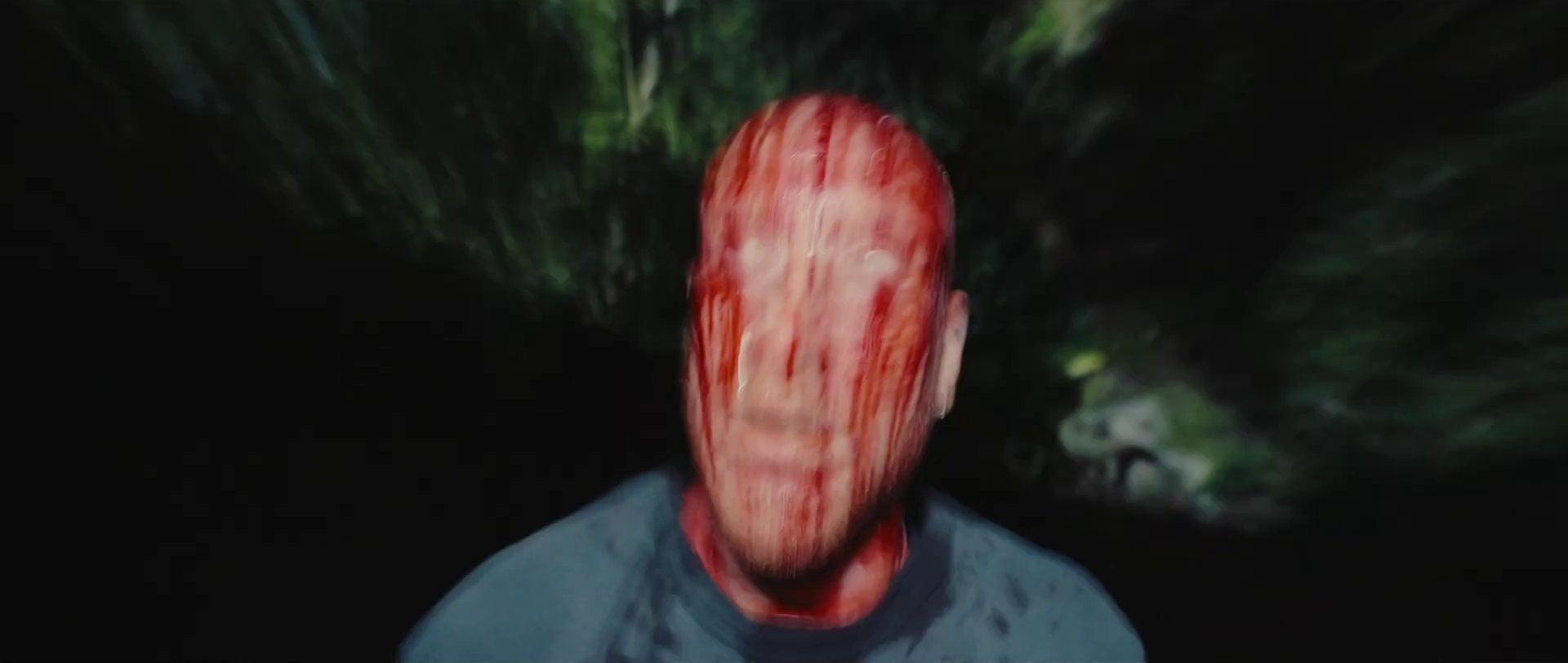 A close, motion-blurred shot of a man's face streaked with blood in the dark.